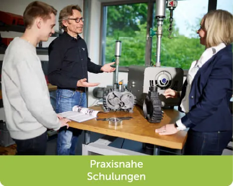 3 Personen stehen an einem Tisch auf denen Teile einer Klauenvakuumpumpe stehen und f&uuml;hren ein Fachgespr&auml;ch
